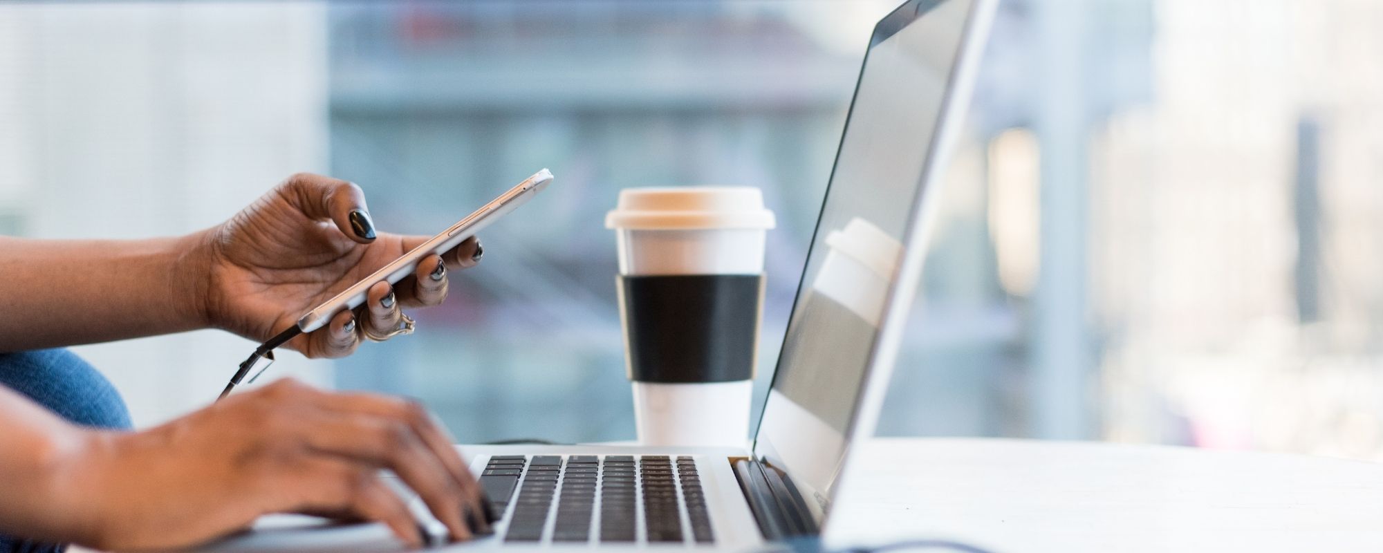 Une personne sur son ordinateur en train d'écrire un message sur son téléphone portable