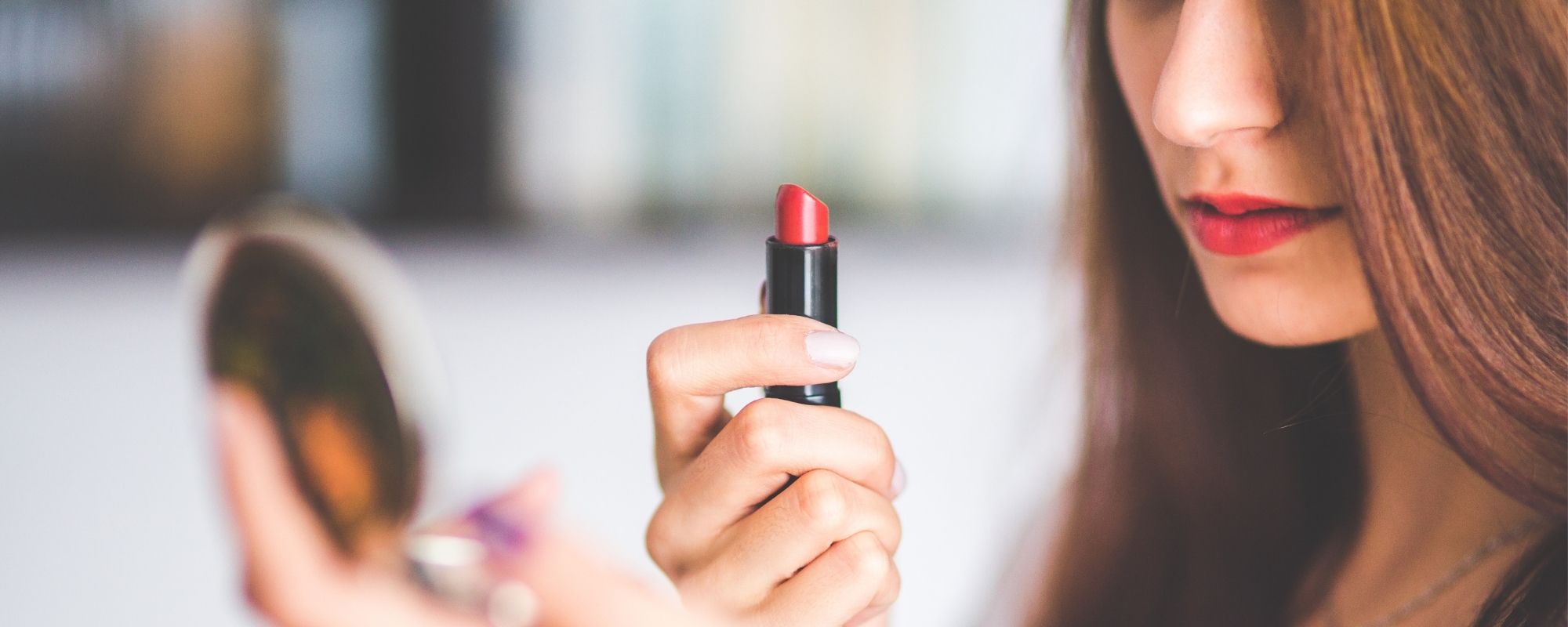 Une femme qui tient un rouge à lèvres de couleur rouge dans la main et se regarde dans le miroir